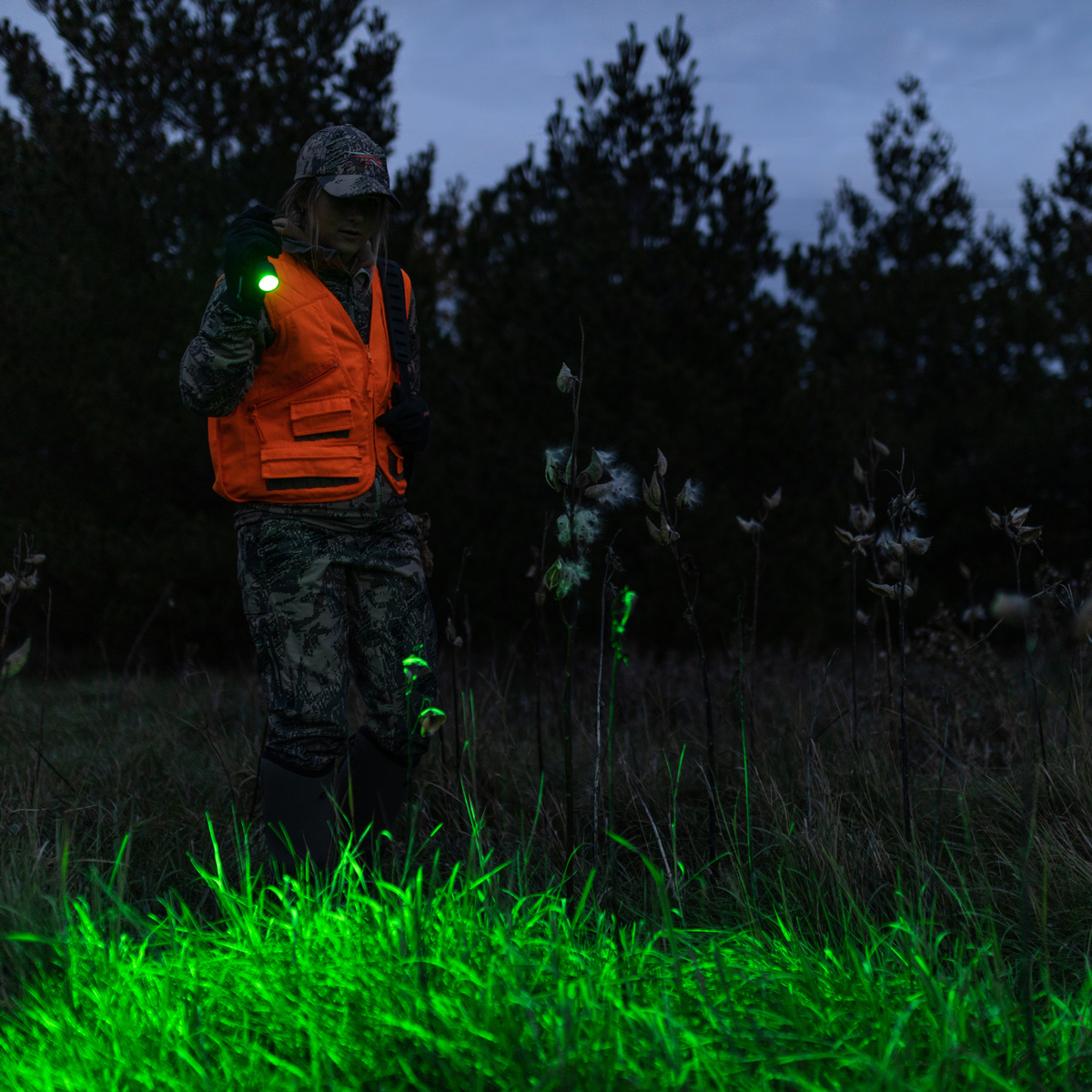 Hunter in blaze orange using a Ledlenser flashlight in the dark woods